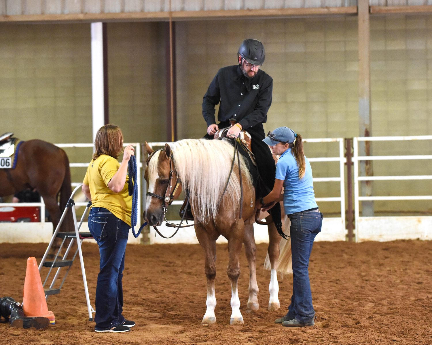 A volunteer helps and EWD rider adjust his stirrups as he prepares to show.